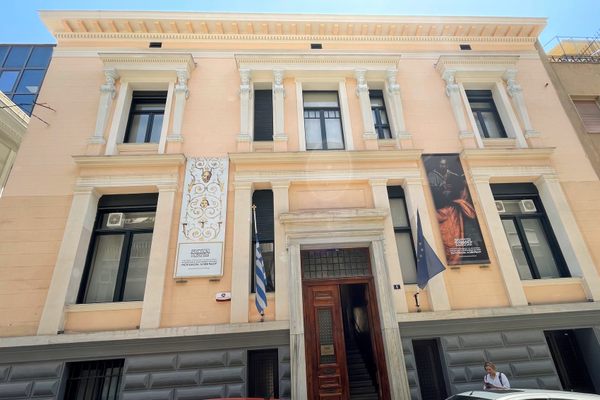 A neoclassical two-floor light pink mansion with five windows and a centered entranceway